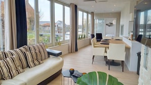 A modern living room with a sofa, dining area, and large windows. - Pura Vida del Rio : Enjoy life ! (Oud Ade)