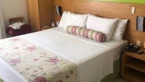 Une chambre d’hôtel avec un lit, des murs verts, une tête de lit en bois et une couvre-lit à motifs floraux.