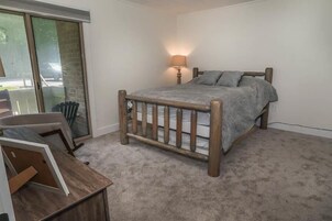 Un dormitorio con cama de madera, una mesita de noche, una lámpara y vistas a través de una puerta corredera de cristal.