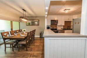 Una cocina moderna con armarios blancos, una isla de madera y un comedor con sillas y mesa de madera.