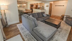 A modern living room with a sectional sofa, a coffee table, and a dining area with chairs and a table.
