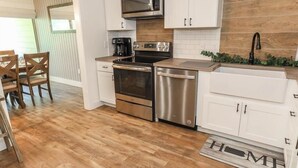 A modern kitchen with stainless steel appliances, white cabinetry, and a wooden floor.