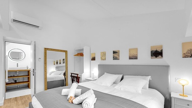 Una habitación de hotel moderna con una cama grande, una mesita de noche con lámpara, un armario, un espejo y obras de arte en las paredes.