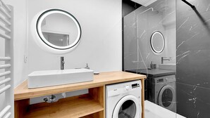 Un baño moderno con un lavabo blanco, espejo redondo y lavadora integrada.
