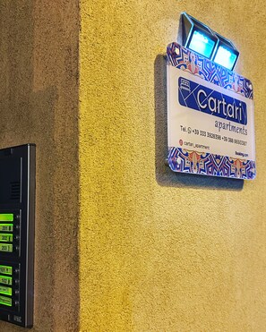 A wall-mounted sign for Cartari apartments with contact information and a booking website. - CARTARI APARTMENT (Palermo)
