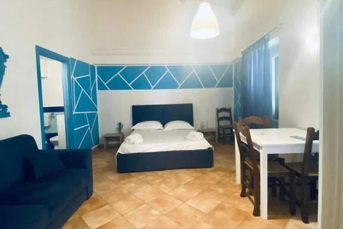 A room with a bed, a sofa, a dining table, and chairs.
