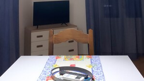A room with a wooden ceiling, a table with a patterned tablecloth, a television on a stand, and a hanging light fixture. - CARTARI APARTMENT (Palermo)