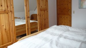 Ein Schlafzimmer mit Holzschrank, einem Einzelbett und einem Sessel.