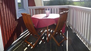 Eine Holzterrasse mit Tisch und Stühlen, einem weißen Geländer und einem Fenster.
