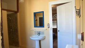 Un baño con ducha, lavamanos y una puerta que da a otra habitación.