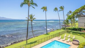 A poolside area with a view of the ocean, palm trees, and a building in the background. - *Lauloa 312* Maui Prime 3 Bedroom Oceanfront Condo (Maalaea)