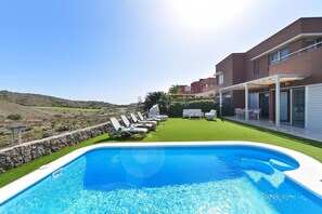 A modern pool area with a clear view of the surrounding landscape, a well-maintained lawn, and a building with a covered patio.