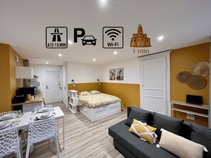 A modern hotel room with a bed, a sofa, a dining area, and a kitchen.