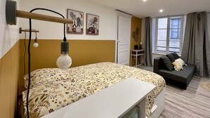 Une chambre à coucher comprenant un lit, une table de chevet, un bureau, un canapé et une fenêtre avec des rideaux.