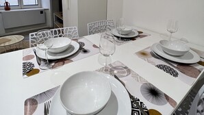 Un coin repas avec une table dressée pour quatre personnes, des chaises blanches et un miroir décoratif accroché au mur.