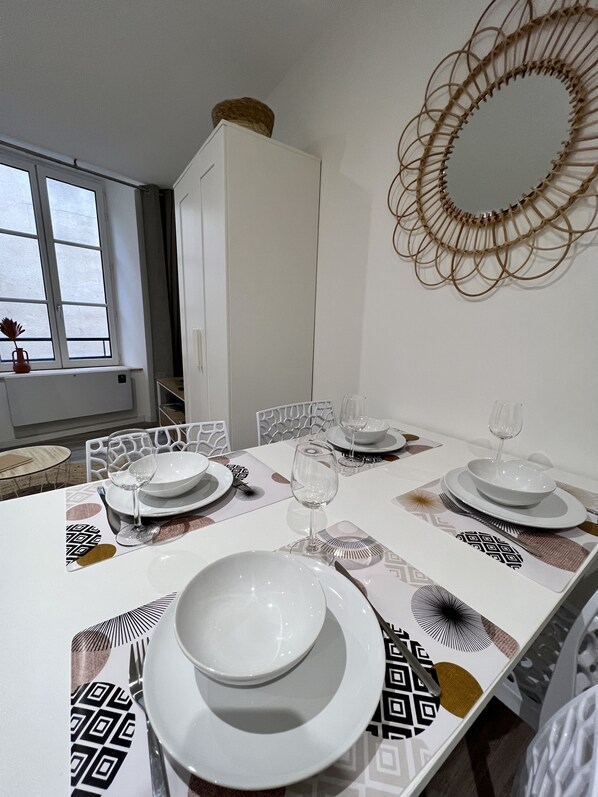 A dining area with a table set for four, white chairs, and a decorative mirror on the wall. - 🌴 La Palmeraie 🌴 (Brioude)