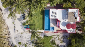 An aerial view of a resort with a swimming pool, multiple lounge chairs, and palm trees. - Quiet Home on Beautiful Private Beach w/ Pool (Tulum)