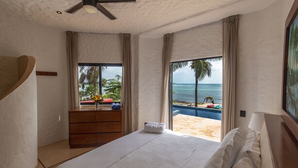 A bedroom with a bed, a dresser, and a view of the beach. - Quiet Home on Beautiful Private Beach w/ Pool (Tulum)