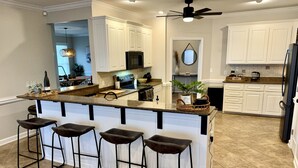 A modern kitchen with white cabinetry, a granite countertop, and a central island with bar stools. - Solaria: Waterfront, Heated Pool, Kayak, Fish/Golf, St George Island (Eastpoint)