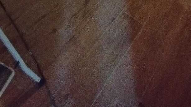 Une pièce avec un plancher en bois, un seul luminaire et une fenêtre dotée d’un cadre sombre.