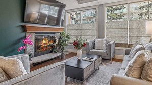 A modern living room with a fireplace, comfortable seating, and large windows.
