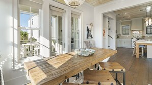 Un comedor espacioso con una mesa de madera y bancos, ventanas grandes y una araña.