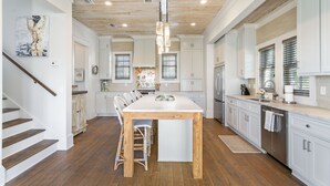 Una cocina amplia con una isla central, suelo de madera, armarios blancos e iluminación colgante moderna.
