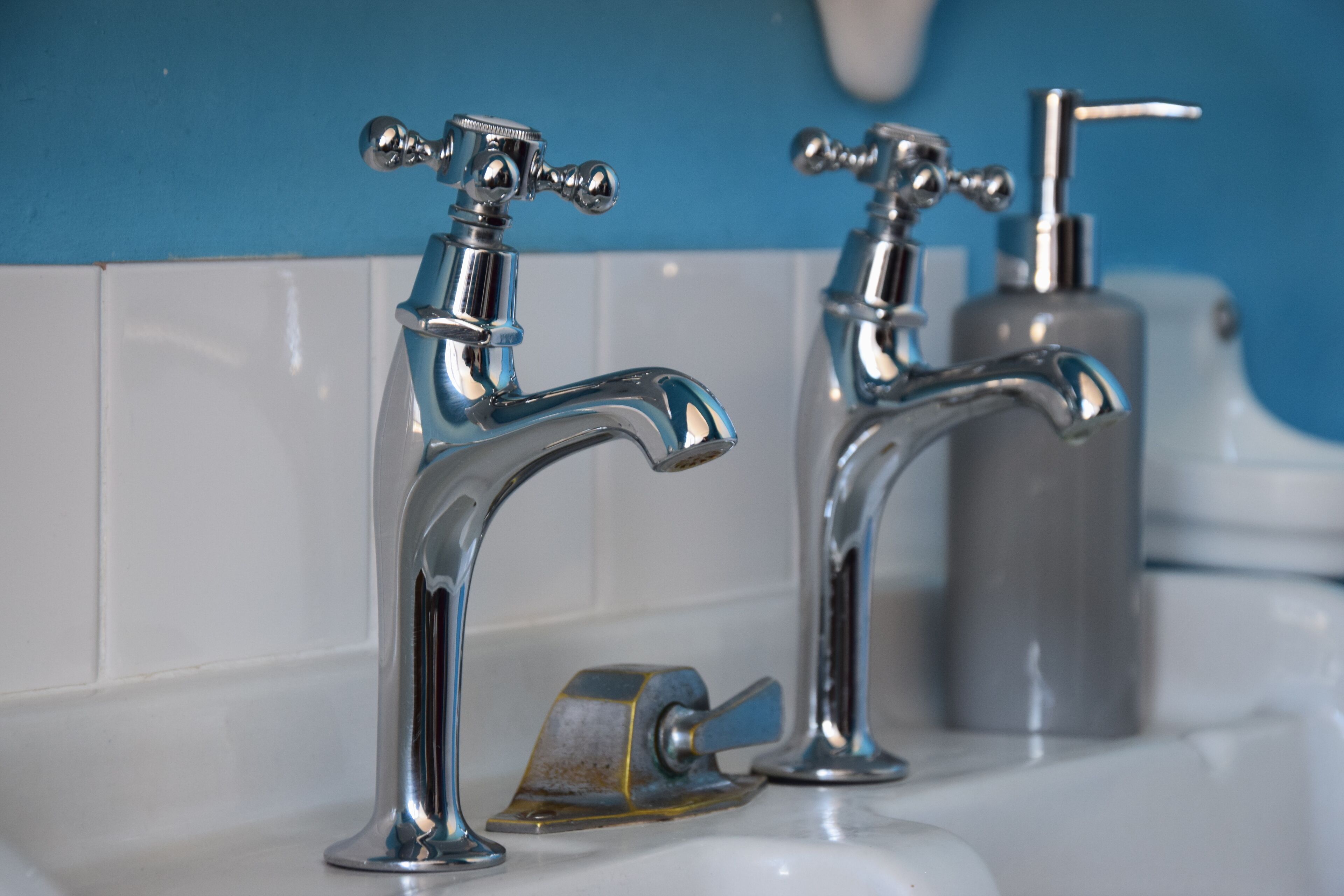 Dos grifos cromados con un dispensador de jabón sobre un lavabo blanco frente a una pared azul.