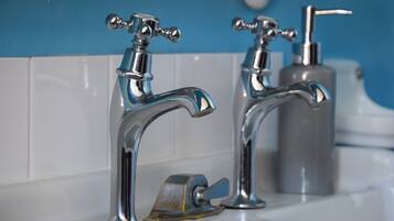 Dos grifos cromados con un dispensador de jabón sobre un lavabo blanco frente a una pared azul.