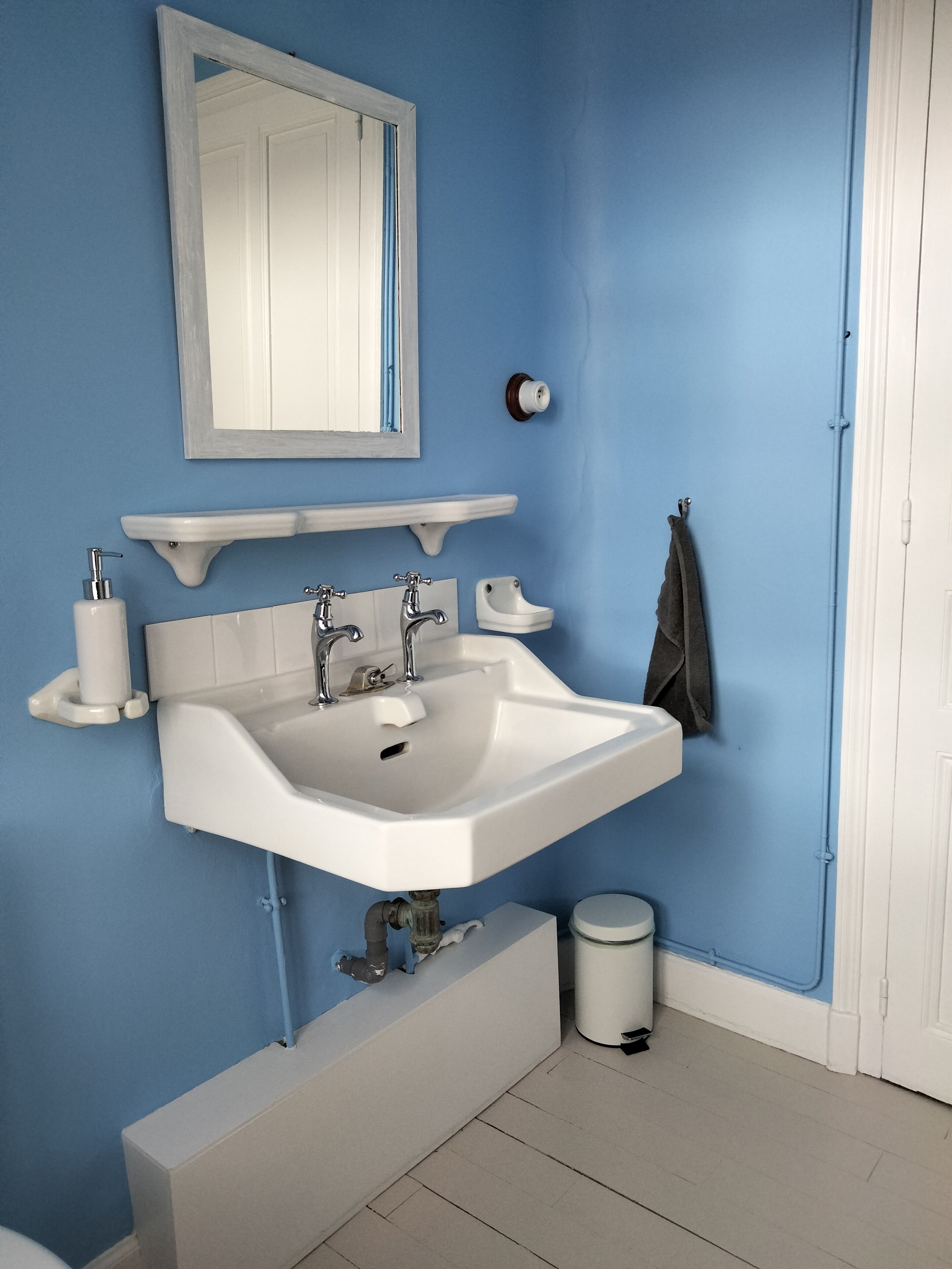 Une salle de bain avec un lavabo blanc, deux robinets, un miroir, un porte-serviettes et des toilettes.