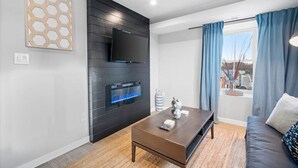 Una sala moderna con un televisor de pantalla plana montado en un panel negro, una chimenea empotrada, una mesa de centro y un sofá.