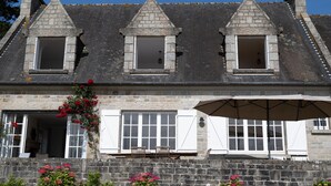 A stone building with three triangular gables, a balcony with chairs, and a large umbrella. - Renovated villa in park, very large sea view, 5 minutes walk from the beach (Saint-Cast-le-Guildo)