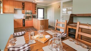 A compact kitchen with wooden cabinets, a dining table set with plates, glasses, and a pitcher. - Marsh Garth (Kirkby-in-Furness)