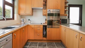 A modern kitchen with wooden cabinets, a built-in oven, a microwave, and a dishwasher. - Marsh Garth (Kirkby-in-Furness)