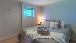 A neatly arranged bedroom with a bed, pillows, a bedside lamp, a small window, and a ceiling light.