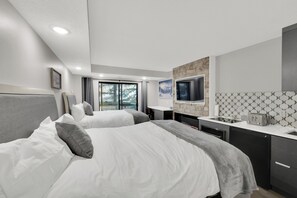 A modern hotel room with two beds, a kitchen area, and a large window.