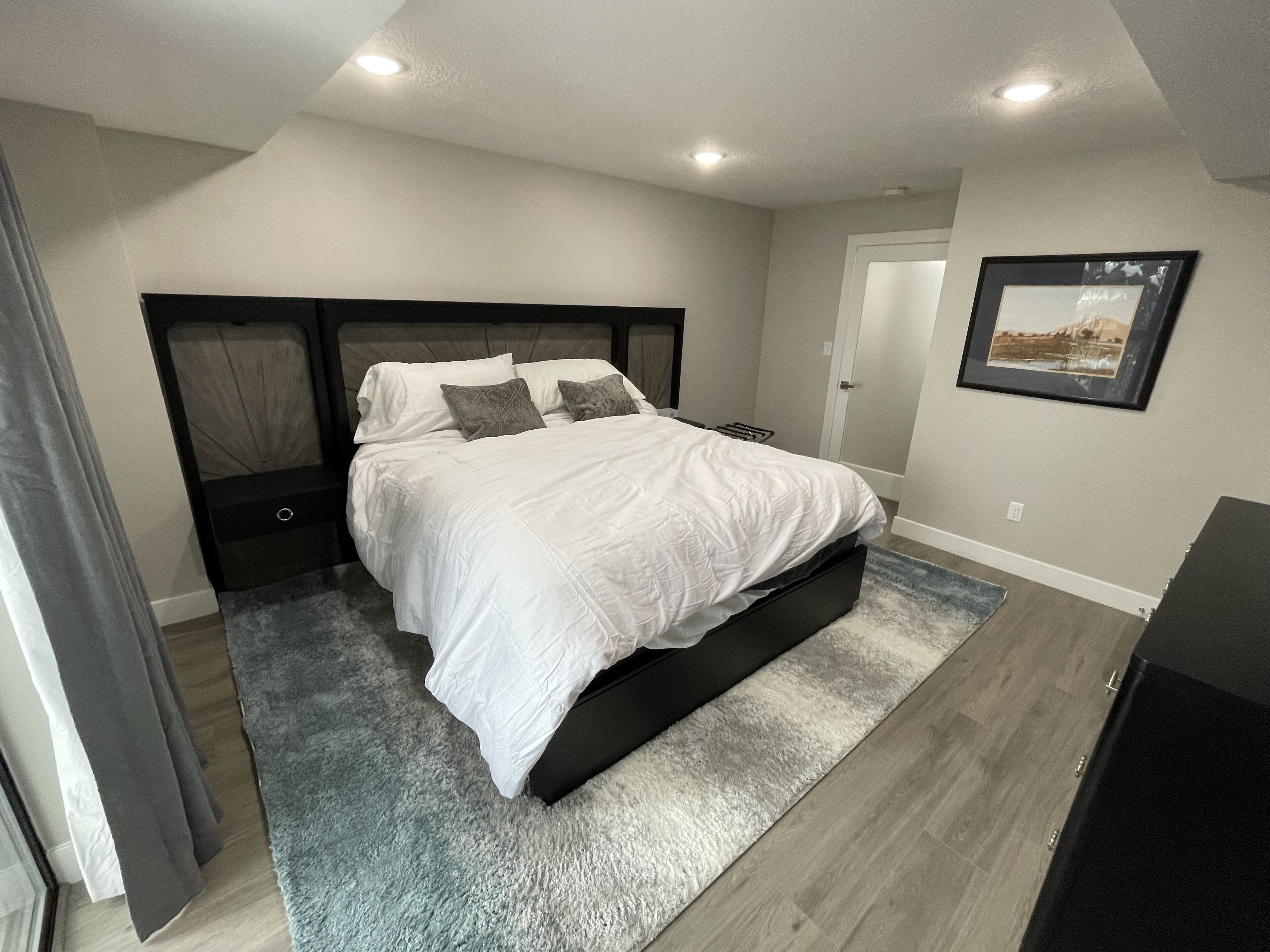 A bedroom with a bed, a headboard, a door, a framed picture on the wall, and a carpet.