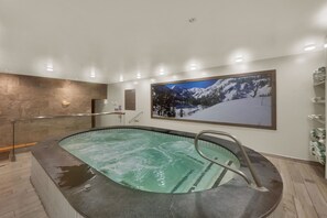 A spa area with a hot tub, wooden flooring, a stone wall, and a large framed picture of a snowy mountain. - Stay next to Park City Resort! Rebuilt 2BR, 2BA Condo, MODEL PERFECT, HOT TUB (Park City)