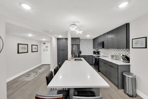 A modern kitchen with a central island, dark cabinetry, and a patterned backsplash.