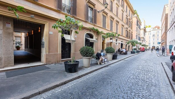 A cobblestone street lined with historic buildings, outdoor seating, and potted plants. - Elegant apartment in Via della Frezza, near Piazza di Spagna / Spanish Steps (Rome)