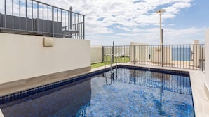 En swimmingpool med fliseterrasse, gelænder og havudsigt.