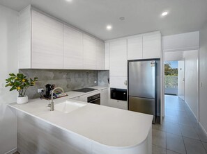Une cuisine moderne avec des meubles blancs, un îlot central, un réfrigérateur en acier inoxydable et un four à micro-ondes.