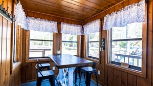 A wooden interior with a table and four chairs, large windows with lace curtains, and a view of the outside. - Comfy pet friendly 2 bedroom with fireplace (Saint Germain)