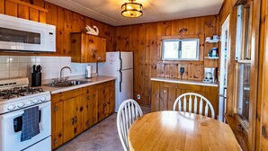 A compact kitchen with wooden cabinets, a microwave, a stove, a refrigerator, and a dining table with chairs. - Comfy pet friendly 2 bedroom with fireplace (Saint Germain)
