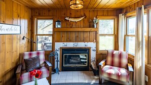 A cozy cabin interior with wooden walls, a fireplace, plaid furniture, and a sign reading "her at the lake". - Comfy pet friendly 2 bedroom with fireplace (Saint Germain)