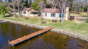 A lakeside cabin with a dock extending into the water, surrounded by trees and a grassy area with picnic tables. - Comfy pet friendly 2 bedroom with fireplace (Saint Germain)