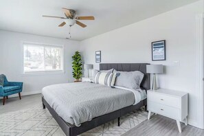 A modern bedroom with a bed, bedside tables, a ceiling fan, a window, and a plant.