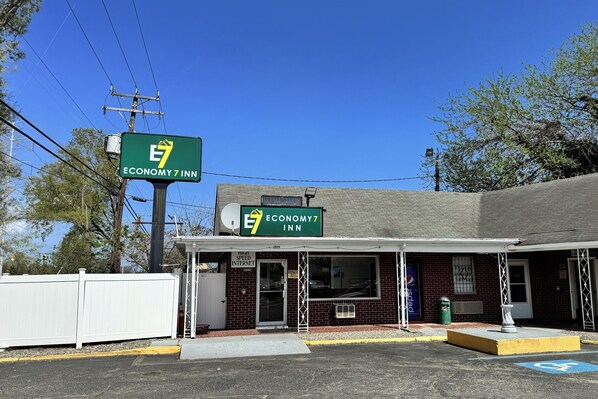 A brick building with a green sign for Economy 7 Inn, a covered entrance, and a parking lot with a handicapped parking space.