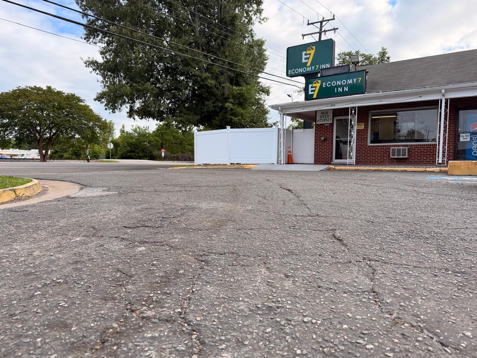 A road leading to Economy 7 Inn with a brick building and a white fence.