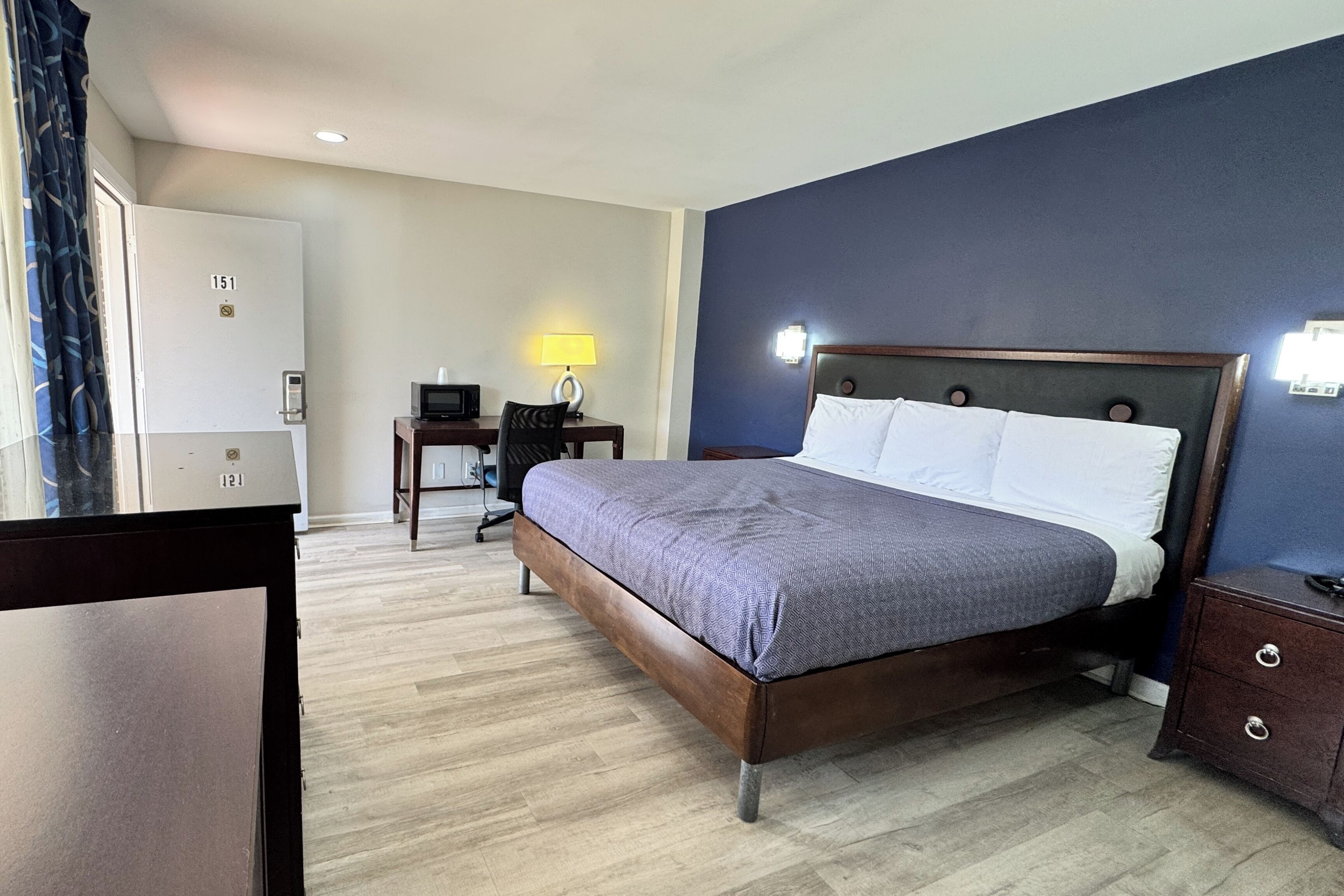 A hotel room with a bed, a desk with a lamp, a chair, and a wardrobe.